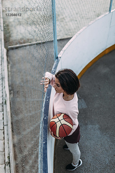 Junge Frau steht mit Basketball am Zaun