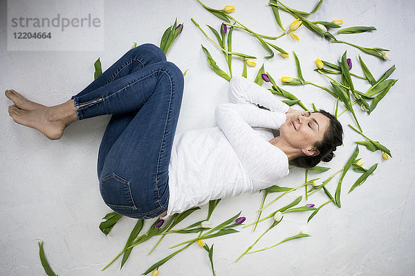 Lächelnde Frau inmitten von Tulpen auf dem Boden liegend