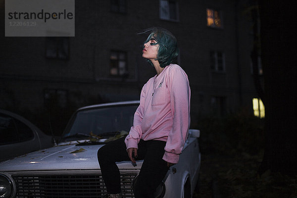 Kaukasische Frau sitzt nachts auf der Motorhaube eines Autos