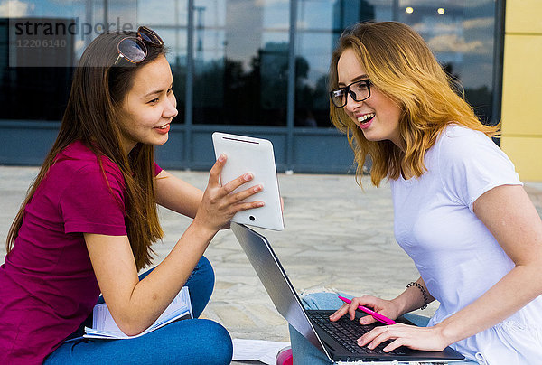 Kaukasische Frauen  die im Freien einen Laptop und ein digitales Tablet benutzen