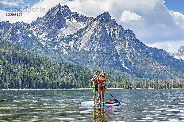 Kaukasisches Paar auf Paddleboard im See