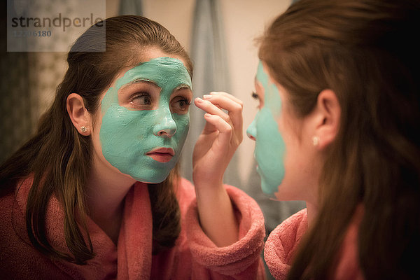 Kaukasisches Mädchen beim Auftragen einer Gesichtsmaske im Spiegel