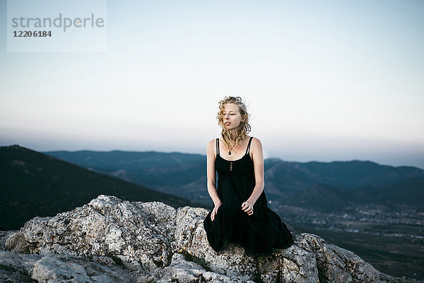 Kaukasische Frau sitzt auf einem Felsen in der Nähe von Bergen