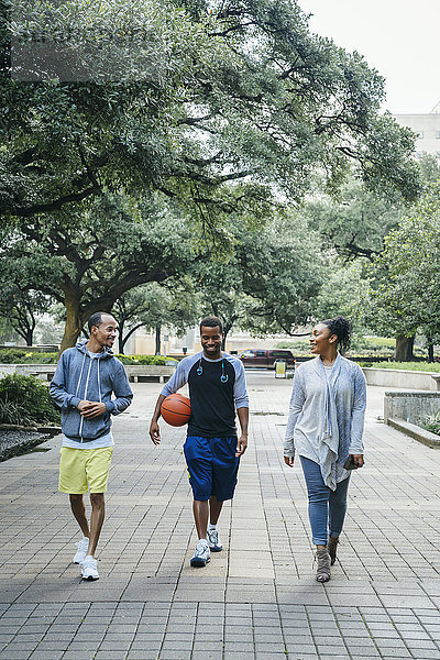 Lächelnde schwarze Freunde gehen im Park mit Basketball
