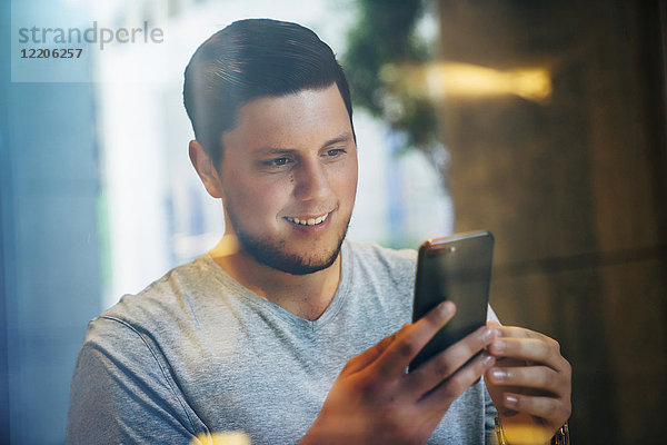 Lächelnder kaukasischer Mann  der eine SMS auf seinem Handy schreibt