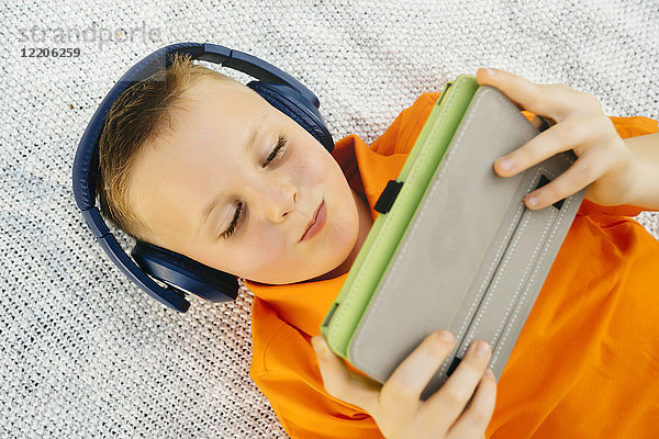 Lächelnder kaukasischer Junge liegt auf einer Decke und hört einem digitalen Tablet zu