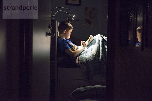 Kaukasischer Junge liest nachts im Bett ein Buch