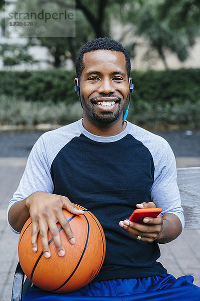 Porträt eines schwarzen Mannes  der Ohrstöpsel hört und einen Basketball hält