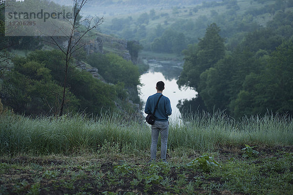 Kaukasischer Mann steht auf einem Hügel über einem Fluss