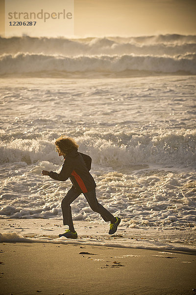 Gemischtrassiger Junge läuft am Strand