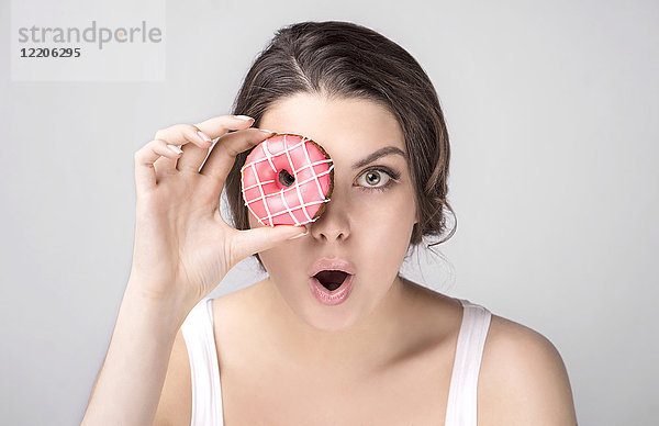 Überrascht Kaukasische Frau hält Donut über Auge