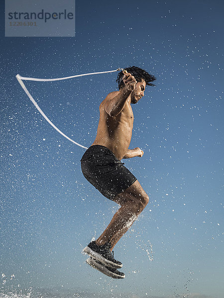 Wasser spritzt auf Hispanic Mann springt Seil