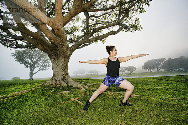 Gemischtrassige Frau  die in der Nähe eines Baumes trainiert und sich streckt