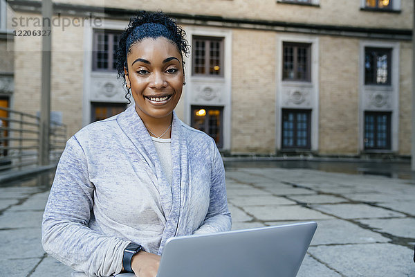 Porträt einer lächelnden schwarzen Frau  die im Freien einen Laptop benutzt