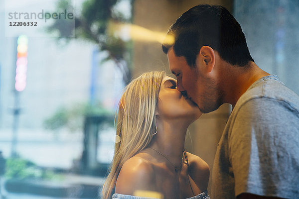 Kaukasisches Paar küsst sich hinter dem Fenster
