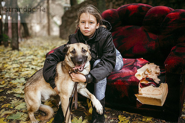 Kaukasische Frau sitzt auf dem Sofa im Freien und umarmt einen Hund