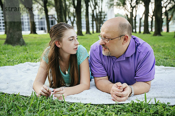 Seriöser kaukasischer Vater und Tochter unterhalten sich auf einer Decke im Park