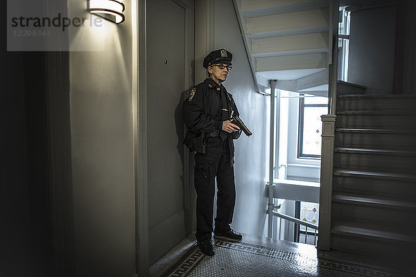 Ältere kaukasische Polizistin mit Waffe im Treppenhaus einer Wohnung