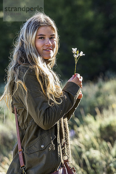 Porträt eines lächelnden kaukasischen Mädchens  das eine Wildblume hält