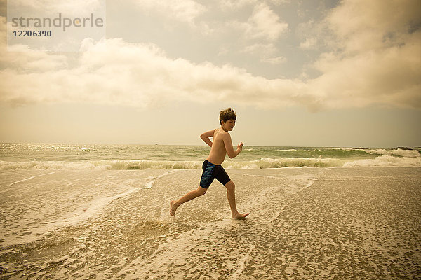 Kaukasischer Junge läuft in den Wellen des Ozeans