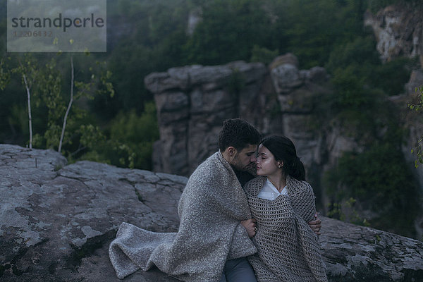 Kaukasisches Paar sitzt auf einem Felsen  eingewickelt in eine Decke