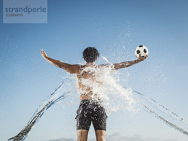 Wasser spritzt auf den Rücken eines hispanischen Mannes  der einen Fußball hält