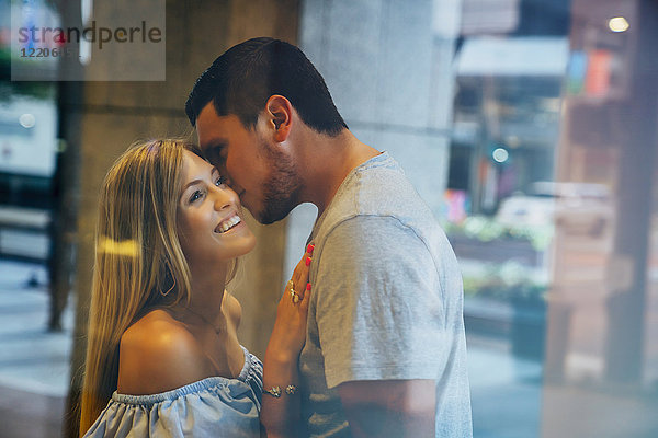 Kaukasischer Mann küsst Frau auf Wange hinter Fenster