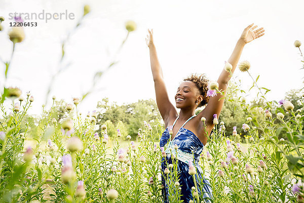 Lächelnde gemischtrassige Frau  die in einem Feld mit Wildblumen feiert