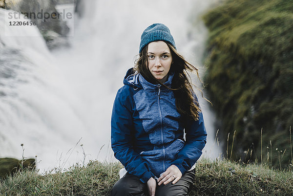 Porträt einer ernsten kaukasischen Frau  die in der Nähe eines Wasserfalls sitzt
