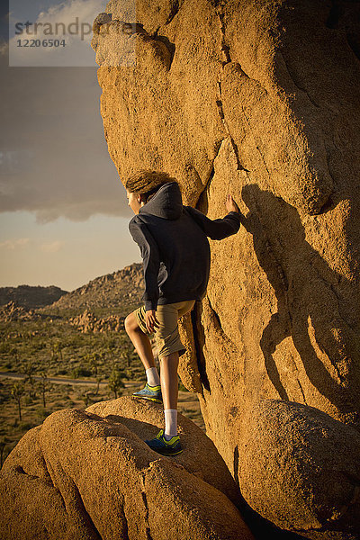 Gemischtrassiger Junge steht auf einem Felsen in der Wüste