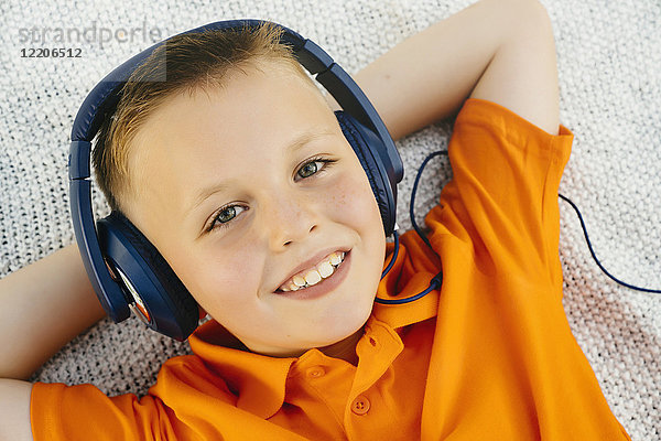 Lächelnder kaukasischer Junge  der auf einer Decke im Park liegt und Kopfhörer hört