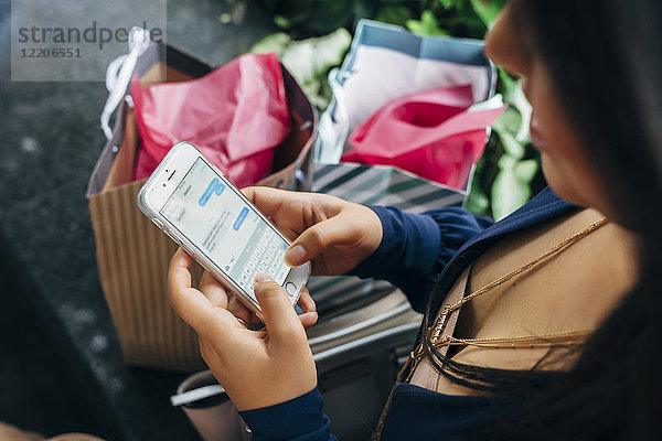 Hispanische Frau mit Einkaufstüten  die eine SMS auf ihrem Handy schreibt