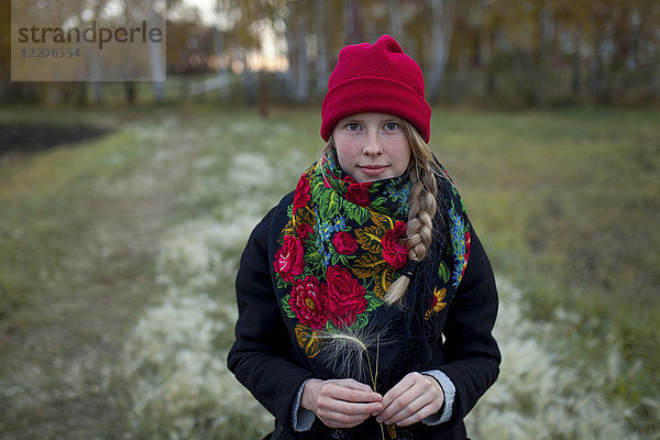 Porträt einer kaukasischen Frau mit Schal und Strumpfmütze  die Heusamen hält