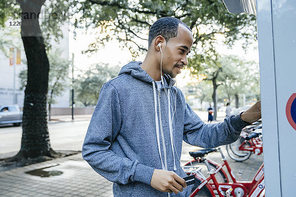 Schwarzer Mann mit Ohrstöpseln  der mit Kreditkarte für einen Fahrradverleih bezahlt
