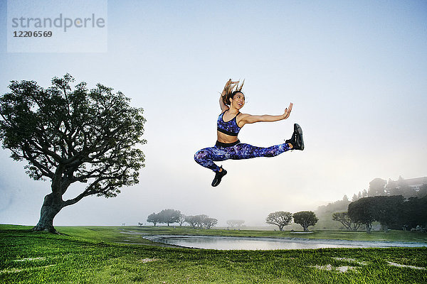 Gemischtrassige Frau  die in der Nähe eines Sees trainiert und springt