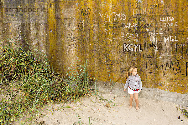 Kaukasisches Mädchen steht im Sand in der Nähe einer Graffiti-Wand