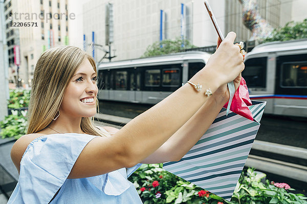 Kaukasische Frau mit Einkaufstasche posiert für Handy-Selfie