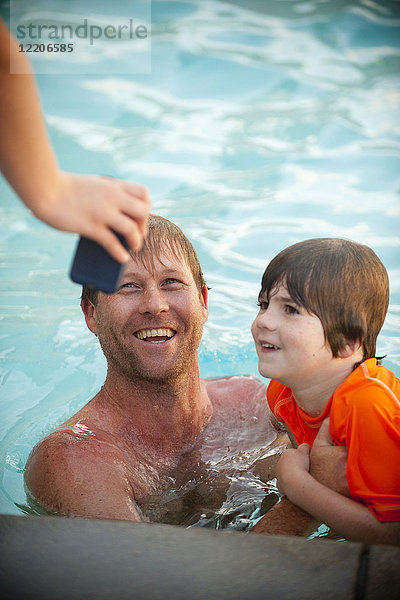 Hand hält Handy für kaukasischen Vater und Sohn im Schwimmbad