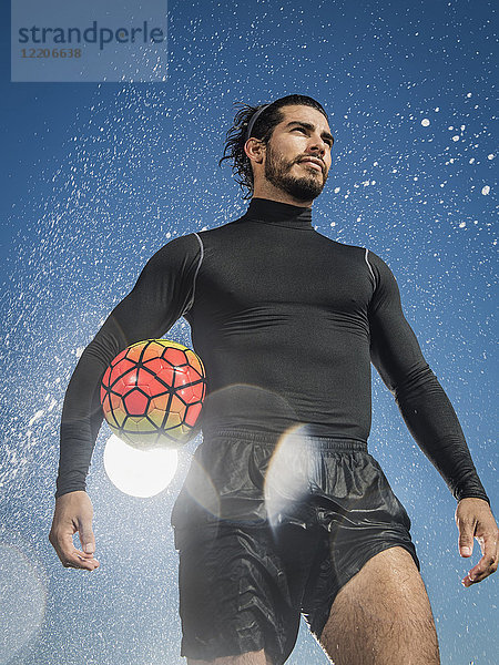 Wasser spritzt auf einen hispanischen Mann  der einen Fußball hält