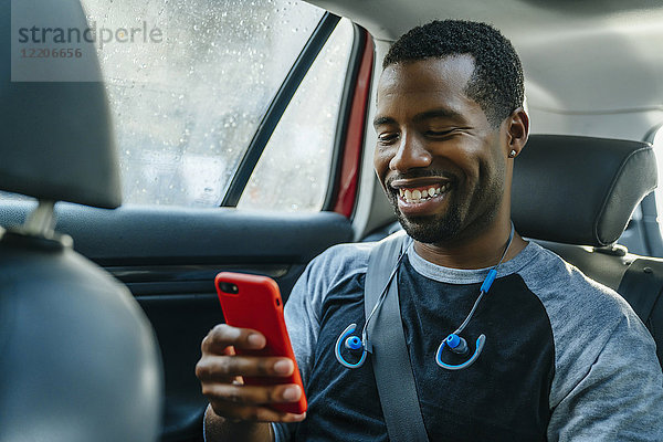 Lächelnder schwarzer Mann  der im Auto eine SMS auf seinem Handy schreibt