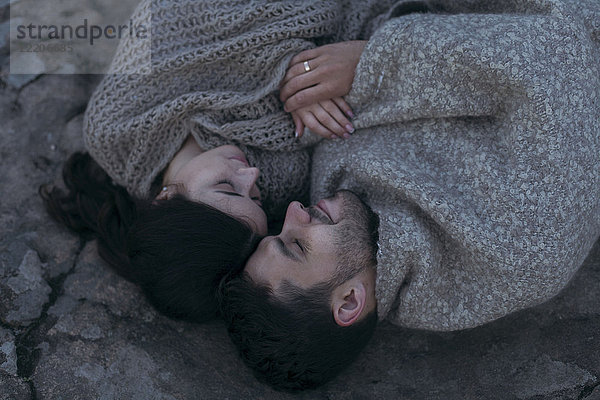 Kaukasisches Paar  das in eine Decke eingewickelt auf einem Felsen liegt