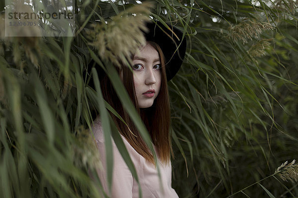Porträt einer ernsten asiatischen Frau  die in einem Feld mit hohem Gras steht