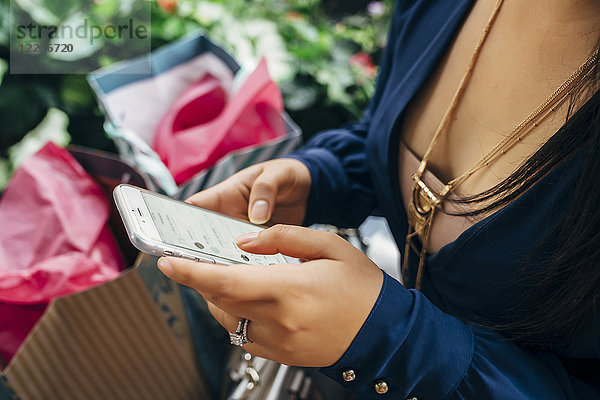 Hände einer hispanischen Frau mit Einkaufstüten  die eine SMS auf ihrem Handy schreibt