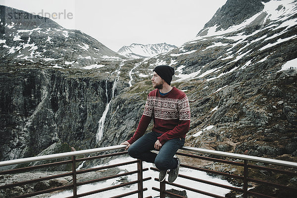 Kaukasischer Mann sitzt auf dem Balkongeländer und bewundert den Schnee auf dem Berg