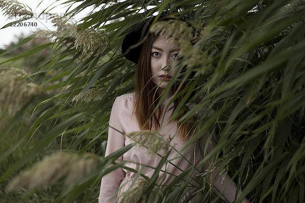 Porträt einer ernsten asiatischen Frau  die in einem Feld mit hohem Gras steht
