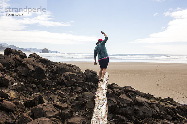 Kaukasische Frau balanciert auf einem Baumstamm auf Felsen am Strand