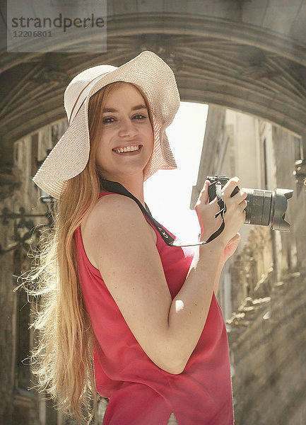 Portrait of smiling Caucasian woman holding camera in city
