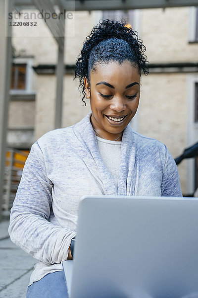 Smiling Black woman using laptop outdoors