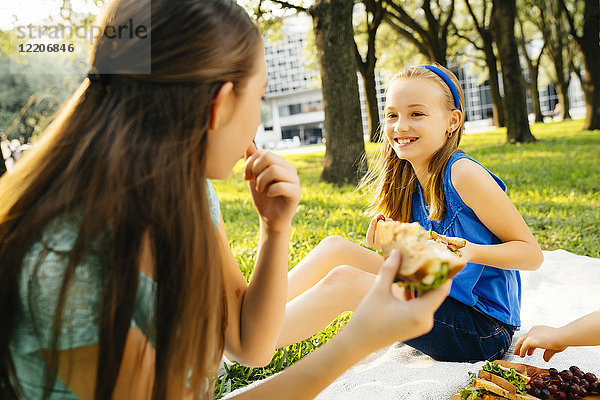 Smiling Caucasian sisters eating food at picnic