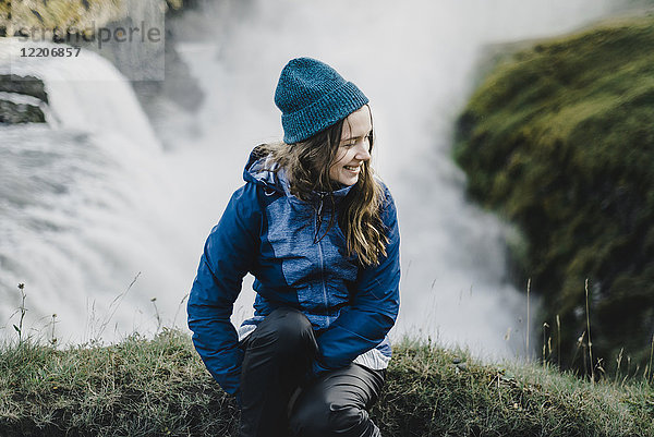 Porträt einer lächelnden kaukasischen Frau  die in der Nähe eines Wasserfalls sitzt